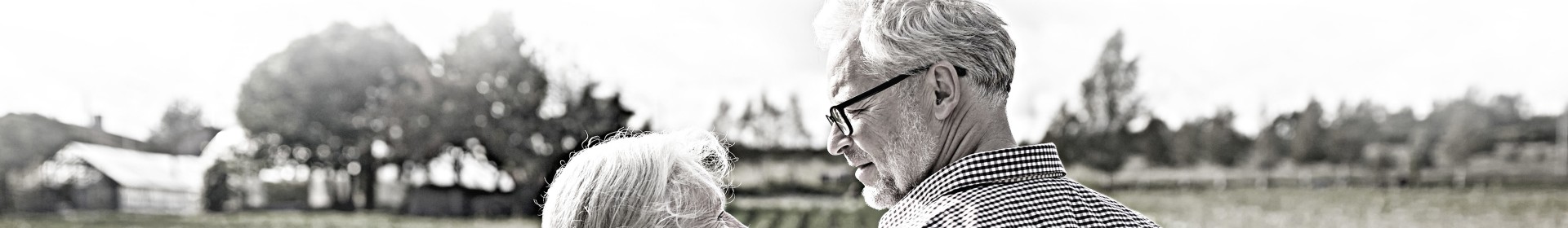 An elderly couple gaze into each others' eyes while standing in front of a field.